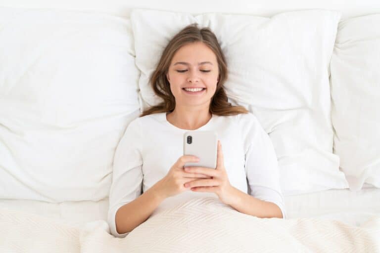 Young female looking at phone screen while lying in bed in morning